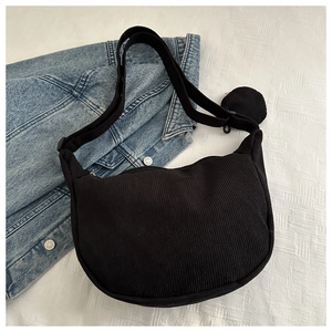 Detail of black corduroy crescent crossbody bag with mini pouch on denim jacket background