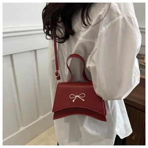 Détail d'un sac à bandoulière rouge avec boucle dorée en nœud et texture en similicuir lisse