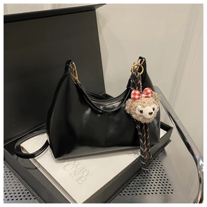 Detail of glossy black moon bag with luxury leather finish and plush bear accessory