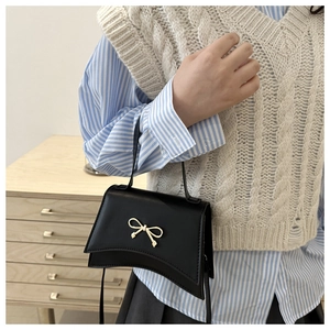 Detail of a black mini crossbody bag featuring a prominent gold bow metal ornament