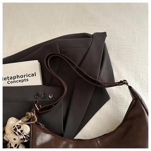 Deep brown crescent shoulder bag with plush bear charm on a minimalist white texture