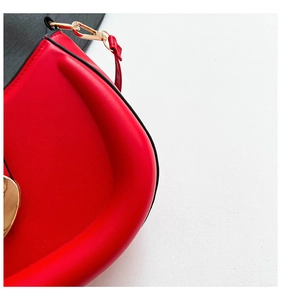 Detailed close-up of a red leather saddle bag featuring a gold heart metal ornament