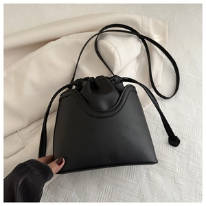 Detail of black drawstring bucket bag in matte leather texture with long shoulder strap