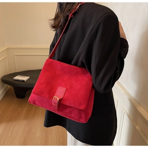 Detail of red suede messenger bag with gold buckle on a model wearing black blazer