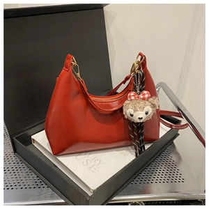 Detail of red glossy crescent shoulder bag with metallic zipper and plush bear charm