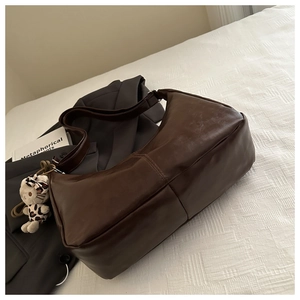 Detail of vintage brown leather hobo bag on white bedding with a cute plush charm