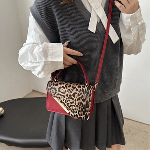 Sac bandoulière rouge avec rabat léopard et barre métallique dorée, porté par un modèle