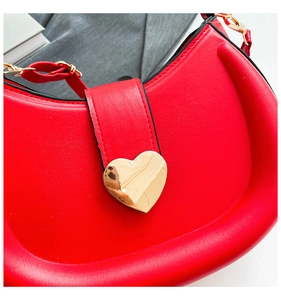 Close-up of a red saddle bag with a large golden heart-shaped metal buckle on smooth leather