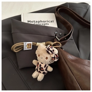 Plush cat charm with leopard dress hanging on a premium dark brown leather tote bag