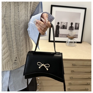 Detail of elegant black square bag featuring a gold bow clasp and sleek leather texture