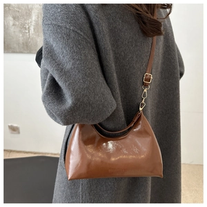 Detail of a dark brown glossy underarm bag showing the oil wax leather texture and strap
