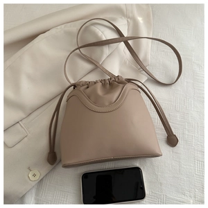 Detail view of a beige drawstring bucket bag with adjustable strap on white fabric