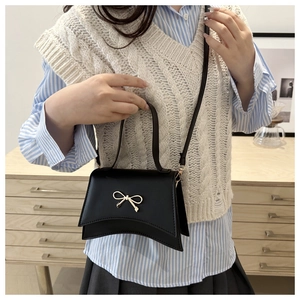 Fashionable black matte handbag with gold bow buckle on model in casual outfit