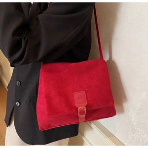 Close-up of red suede messenger bag with gold buckle on a model wearing a blazer