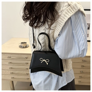 Detail of black trapezoid bag with gold bow clasp worn with striped casual outfit