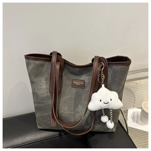 Detail of charcoal canvas tote bag with brown leather trim and white plush charm