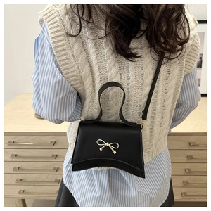 Detail of a black mini crossbody bag with a golden bow clasp on a model in a cafe