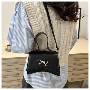 Detail of a black crossbody bag featuring a golden bow ornament and a unique curved base