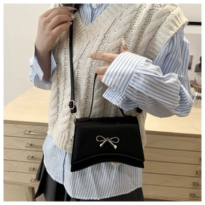 Détail d'un mini sac bandoulière noir avec nœud doré sur cuir mat texturé