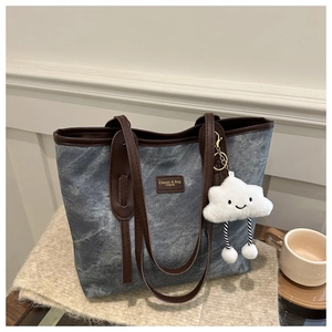 Detailed close-up of a blue denim tote bag with leather handles and a plush cloud charm