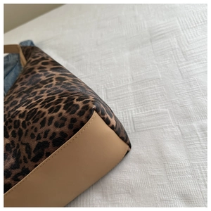 Détail de l'imprimé léopard et base en cuir beige avec coutures fines sur le sac cabas