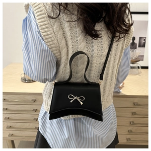 Detail view of the black bow-tie crossbody bag with elegant gold clasp on a model