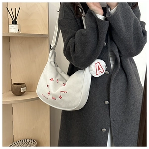 Detail of white corduroy crescent bag with red lettering and detachable coin pouch charm