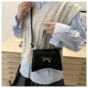 Detail of black crossbody bag with gold bow clasp and elegant matte leather finish