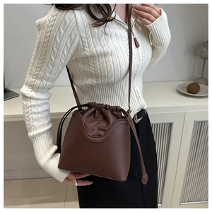 Close-up of a brown leather bucket bag with drawstring closure worn by a model in casual setting