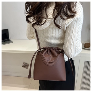 Rear view of model wearing dark brown drawstring bucket bag with adjustable strap