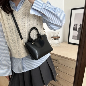 Mini sac seau noir minimaliste avec poignée tressée présenté dans une photo lifestyle miroir