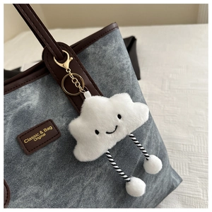 Close-up of a white plush cloud charm with embroidery on a textured tote bag