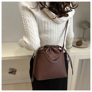 Brown drawstring bucket bag with curved stitching shown on model in a warm indoor setting