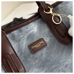 Close-up of washed denim tote bag with brown leather trim and golden metal hardware