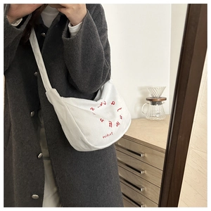 Detailed close-up of white corduroy crescent bag with red Fashion letter embroidery