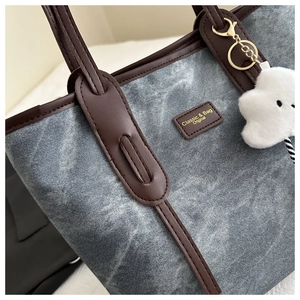 Detail of gray-blue denim tote bag with brown leather trim and fluffy cloud charm