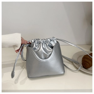 Detail of silver metallic drawstring bucket bag with dual-layer structure on white desk