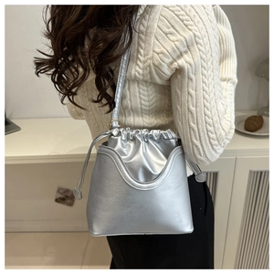 Close-up of a silver metallic drawstring bucket bag worn by a model in a cozy sweater