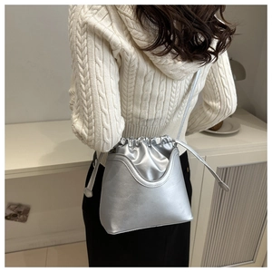 Silver metallic drawstring bucket bag shown worn crossbody over a beige sweater