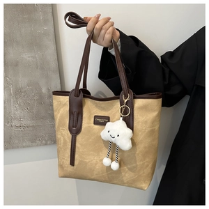 Detail of khaki tote bag with brown leather handles and a plush cloud charm accessory