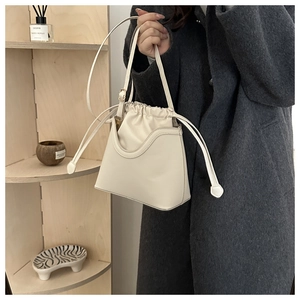Close-up of cream white drawstring bucket bag with wave edge and adjustable strap