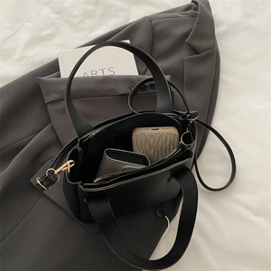 Elegante borsa a secchiello in pelle nera con dettagli dorati su blazer grigio e tessuto