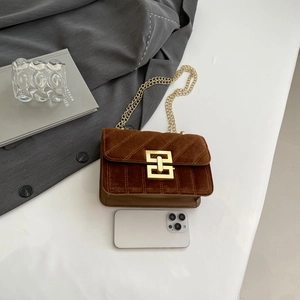 Sac à bandoulière en velours marron avec chaîne dorée et fermoir carré près d'un téléphone