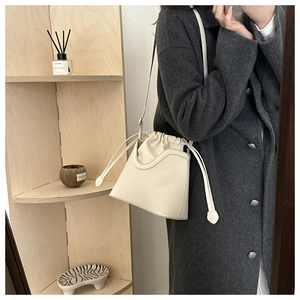 Detail of minimalist cream bucket bag showing wave-cut rim and drawstring inner pouch