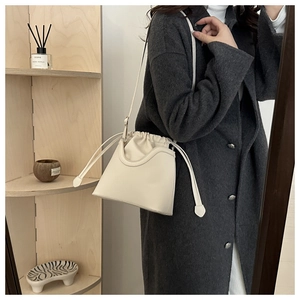 Detail of a minimalist cream-colored bucket bag with U-shaped trim and adjustable strap