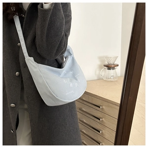 Detail of light blue corduroy crescent bag with 'Fashion' embroidery worn over grey coat