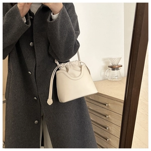Close-up of a minimalist cream leather bucket bag with a stylish drawstring closure