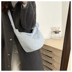 Detail of light blue corduroy shoulder bag with white embroidery on a textured surface