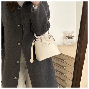 Detail of cream drawstring bucket bag with U-shaped stitching on grey wool coat