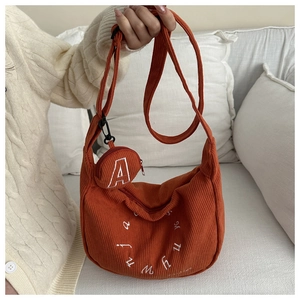 Detail of orange corduroy crescent bag with adjustable strap and small round letter coin pouch